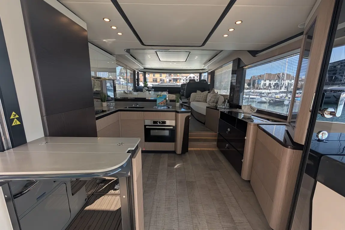 Modern boat interior featuring a kitchen with an oven, sleek cabinetry, and a view of the marina through large windows.